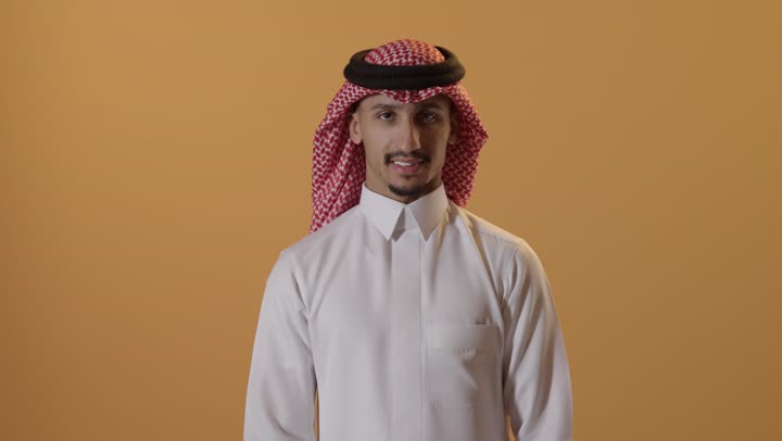 Excellence, distinction, and success, a close-up portrait of a Saudi Arabian Gulf man wearing traditional attire and a ghutrah, raising his thumbs up, gestures of happiness, admiration, and approval, a finger movement indicating acceptance and satisfaction, with an orange background.