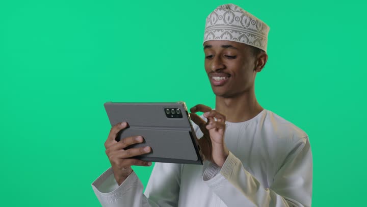 رجل عماني يستخدم جهاز لوحي أمام خلفية خضراء