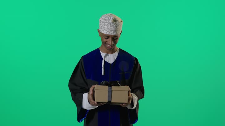 خريج عماني يحمل هدية أمام شاشة خضراء
