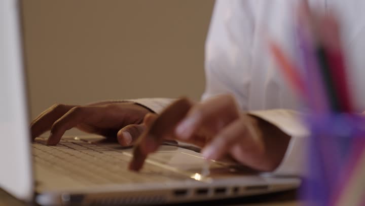 A young Omani is typing on a laptop in a close-up shot.