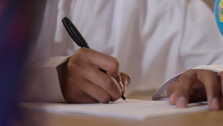A young Omani writes on paper, close-up shot.