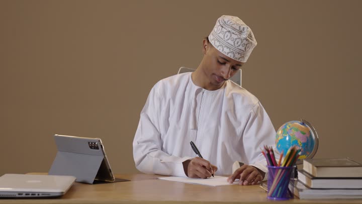 Omani Man Writing at Office Desk with Tablet and Globe