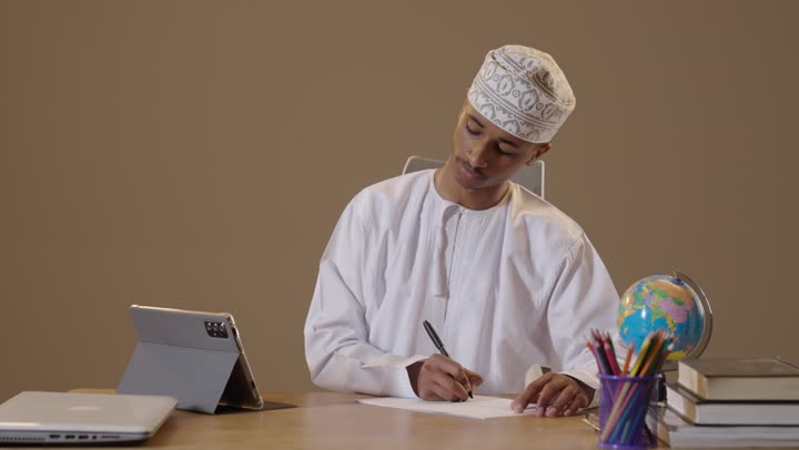 شاب عماني يدرس على المكتب باستخدام الجهاز اللوحي والقلم