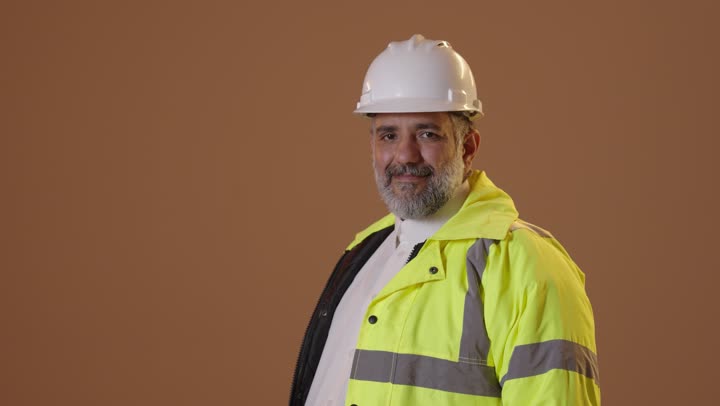 The concept of engineering and architectural construction, a portrait of a Saudi Gulf Arab engineer wearing a helmet and safety vest, smiling and looking at the camera, standing with crossed arms, working in the engineering field, beige background.