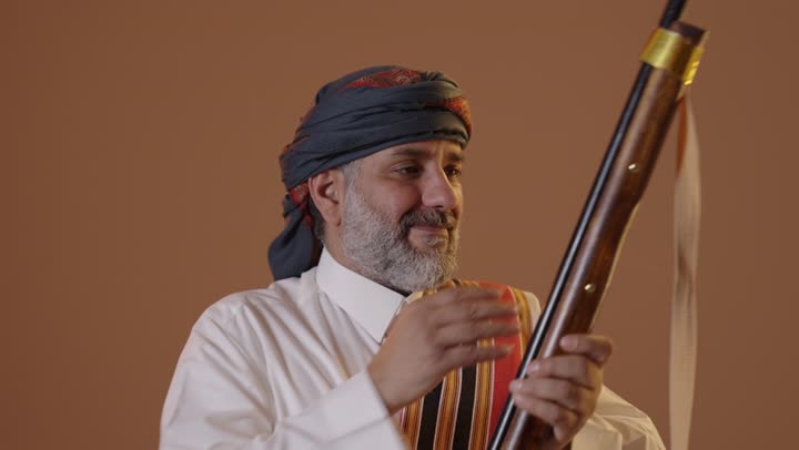 Wearing the traditional attire of the southern region to celebrate national occasions, on the day we began in 1727, a portrait of a smiling Saudi Arabian Gulf man dressed in a thobe and ghutrah with a southern shawl holding a rifle in his hand, commemorating the founding of the first Saudi state on February 22, beige background.