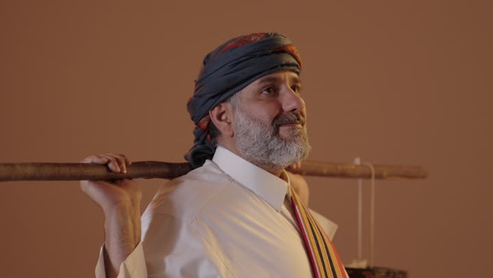 تأسيس الدولة السعودية الاولى 22فبراير، سقاي الماء يقوم بالتجول لسقي الناس من البئر، ارتداء ازياء المنطقة الجنوبية، يوم بدينا 1727م، بورتريه لرجل كبير بالسن عربي خليجي سعودي يرتدي الثوب والغترة والشال الجنوبي يحمل دلو من الجلد,  خلفية بيج