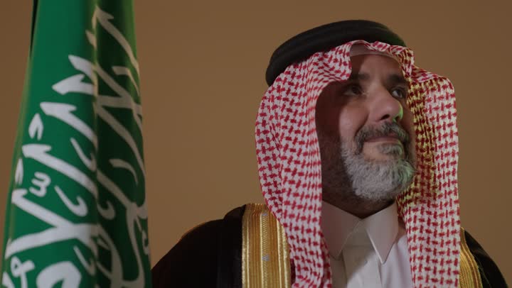 ارتداء الزي الشعبي في مناسبة وطنية,مفهوم حب الوطن والانتماء اليه, يوم بدينا 22 فبراير, ذكرى تأسيس الدولة السعودية الأولى1727م, بورتريه لرجل كبير بالسن عربي خليجي سعودي يرتدي الثوب التقليدي والعقال يمسك علم يوم التأسيس بتعابير الشموخ والفخر، خلفية بيج