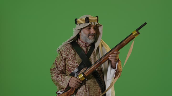The concept of love for the homeland and belonging to it, the day we started on February 22, wearing traditional attire on a national occasion, the anniversary of the establishment of the first Saudi state in 1727, a portrait of an elderly Arab Gulf Saudi man wearing a bisht and agal standing and holding a Saudi rifle, green background, chroma.