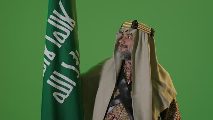 مفهوم حب الوطن والانتماء اليه, يوم بدينا 22 فبراير, ذكرى تأسيس الدولة السعودية الأولى1727م, ارتداء الزي الشعبي في مناسبة وطنية, بورتريه لرجل كبير بالسن عربي خليجي سعودي يرتدي الثوب التقليدي والعقال يمسك علم يوم التأسيس بتعابير الشموخ والفخر، خلفية خضراء، كروما