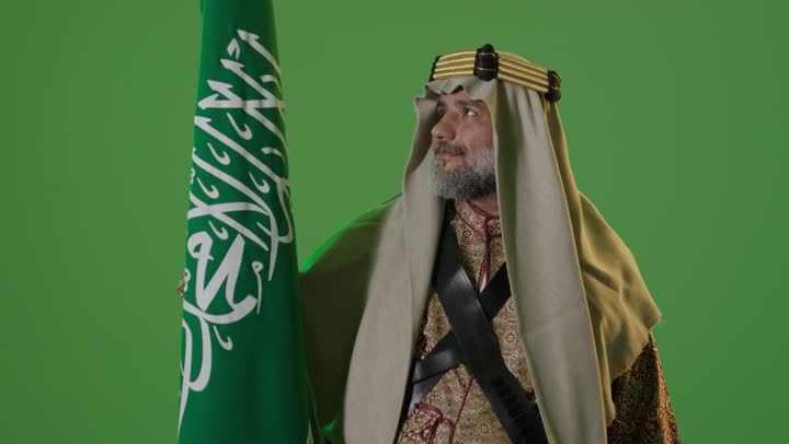 Anniversary of the establishment of the first Saudi state 1727 AD, the concept of love for the homeland and belonging to it, the day we started February 22, wearing traditional attire on a national occasion, a portrait of an elderly Arab Gulf Saudi man wearing traditional thobe and agal holding the flag of the founding day with expressions of pride and dignity, green background, chroma.