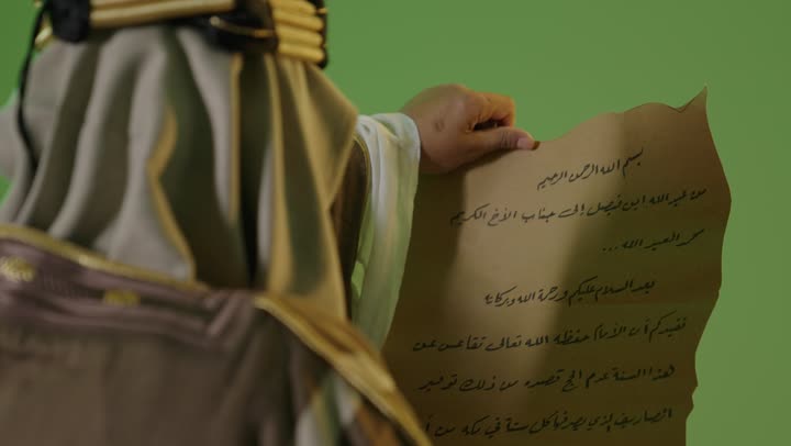 Heritage and authenticity among Arabs, the concept of love for the homeland and belonging to it, the day we started on February 22, the anniversary of the founding of the first Saudi state in 1727, wearing traditional attire on a national occasion, a portrait of an elderly Arab Gulf Saudi man wearing traditional dress and a headband reading a historical leather manuscript, green background, chroma.