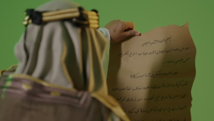 بورتريه  لرجل كبير بالسن عربي خليجي سعودي يرتدي الثوب التقليدي والعقال يقوم بقراءة مخطوطة جلد تاريخية، العراقة والاصالة عند العرب، مفهوم حب الوطن والانتماء اليه, يوم بدينا 22 فبراير, ذكرى تأسيس الدولة السعودية الأولى1727م, ارتداء الزي الشعبي في مناسبة وطنية, خلفية خضراء، كروما