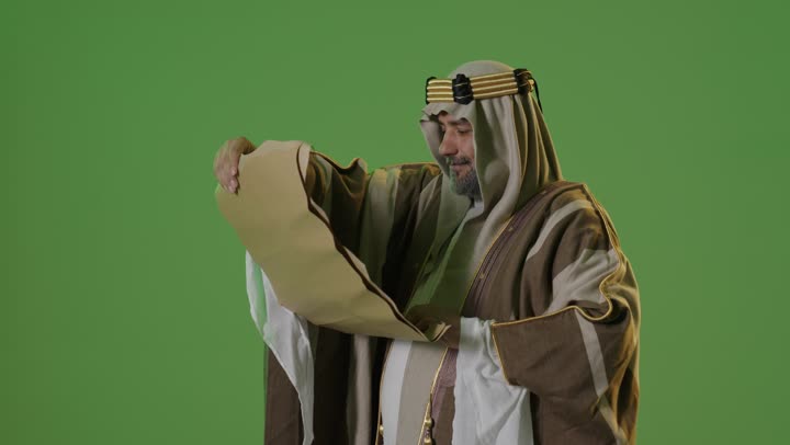 Heritage and authenticity among Arabs, the concept of love for the homeland and belonging to it, the day we started on February 22, the anniversary of the founding of the first Saudi state in 1727, wearing traditional attire on a national occasion, a portrait of an elderly Arab Gulf Saudi man wearing traditional dress and a headband reading a historical leather manuscript, green background, chroma.