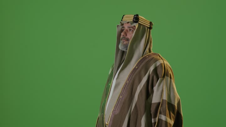 Wearing traditional attire on a national occasion, the anniversary of the establishment of the first Saudi state in 1727, the concept of love for the homeland and belonging to it, the day we started, February 22, a side portrait of an elderly Arab Gulf Saudi man wearing a bisht and agal looking with expressions of pride, green background, chroma.