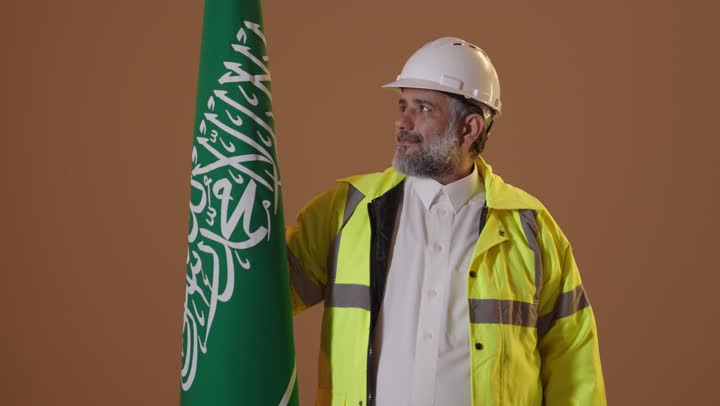 The concept of love for the homeland and belonging to it, on the day we started, February 22, the anniversary of the founding of the first Saudi state in 1727, a portrait of an elderly Arab Gulf Saudi engineer wearing a jacket and a safety helmet holding the flag of the founding day with expressions of pride and dignity, beige background.