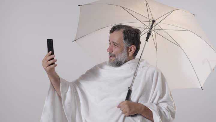 Pilgrim in Ihram with Umbrella Taking Smartphone Selfie