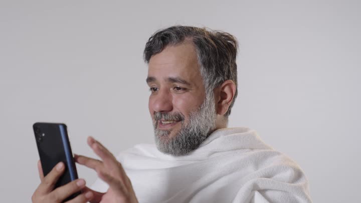 رجل عربي بملابس الإحرام يستخدم مكالمة فيديو بالهاتف