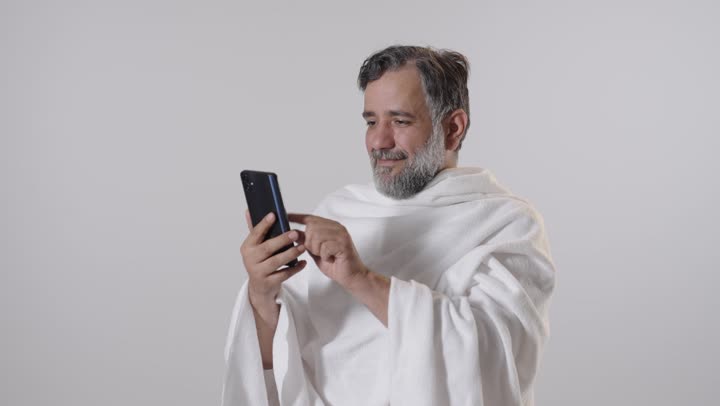 رجل بملابس الإحرام يستخدم الجوال بخلفية بيضاء