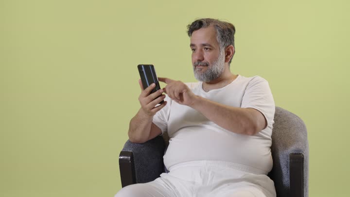 An Arab man using a smartphone against a yellow background.
