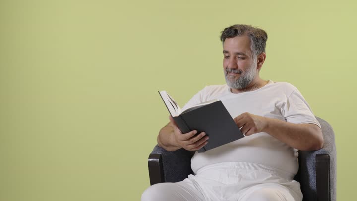 An Arab man reading a book in front of a yellow background, still shot.