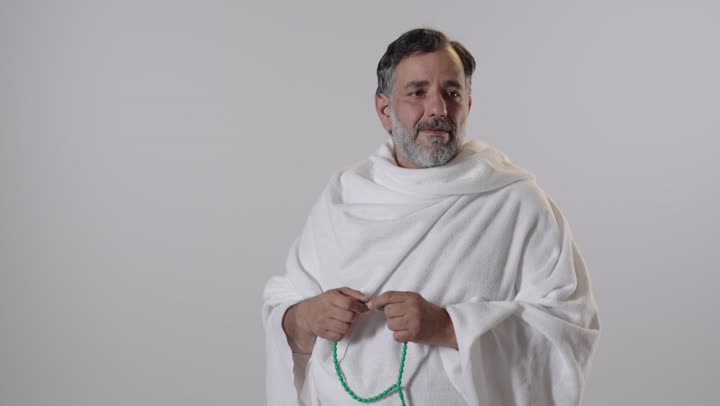 رجل عربي بملابس الإحرام يحمل مسبحة في الاستوديو