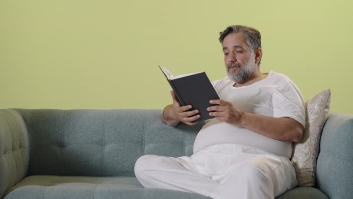 Middle Eastern Man Reading Book on Sofa Indoor Footage