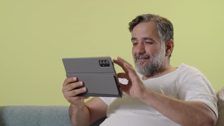 رجل عربي يستخدم جهازاً لوحياً على الأريكة في المنزل