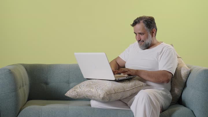 رجل عربي يستخدم الكمبيوتر المحمول على الأريكة