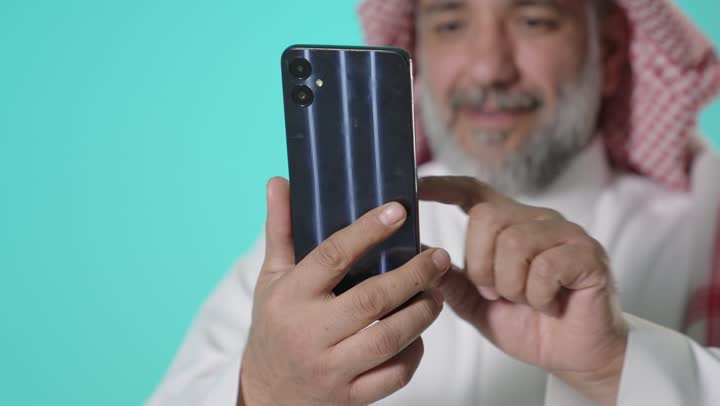 رجل سعودي مسن يستخدم الهاتف الذكي بخلفية تركواز