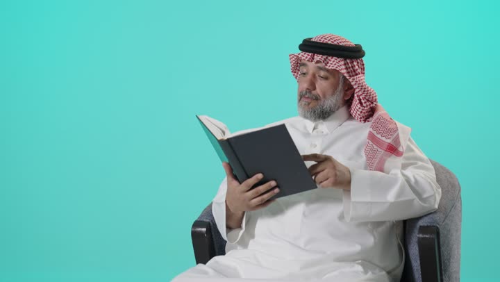 رجل سعودي بالزي التقليدي يقرأ كتاباً في الاستوديو