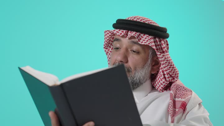 رجل سعودي يقرأ كتاباً أمام خلفية زرقاء