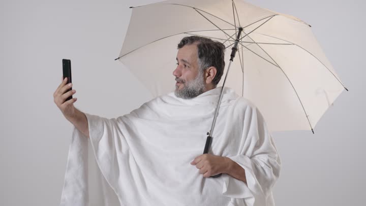 حاج عربي بملابس الإحرام يستخدم الهاتف في الاستوديو