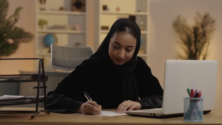 امرأة سعودية تعمل على المحمول وتكتب في المكتب