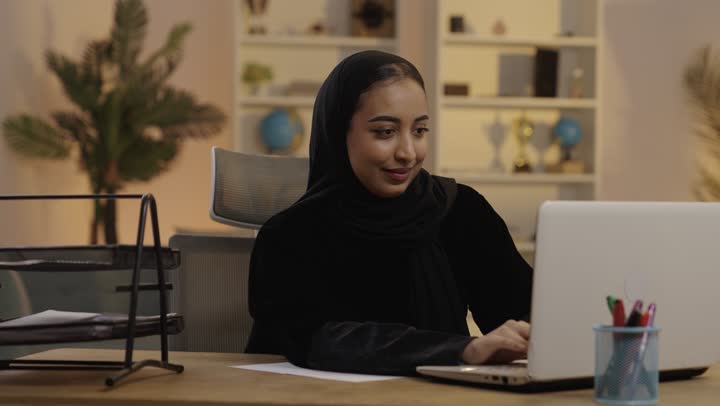 امرأة سعودية تعمل على المحمول وتكتب في المكتب المنزلي