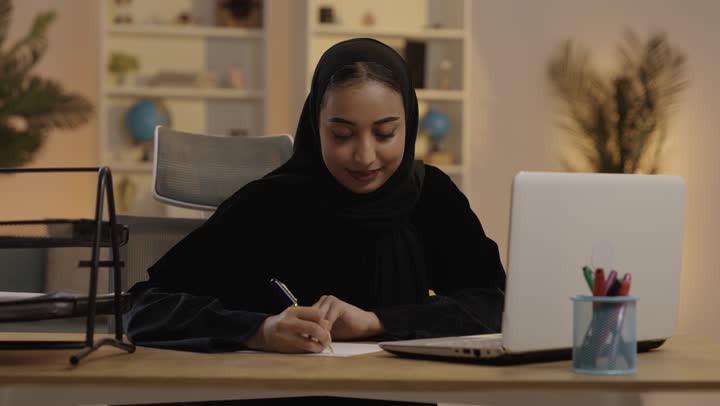 امرأة سعودية تعمل على الكمبيوتر المحمول وتكتب بالمكتب