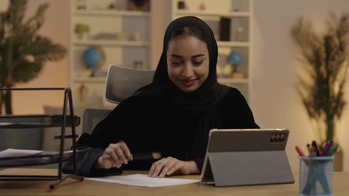 Saudi Woman Writing at Desk with Tablet
