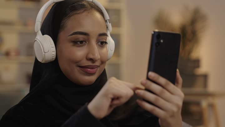 Saudi Woman Using Smartphone with White Headphones at Night