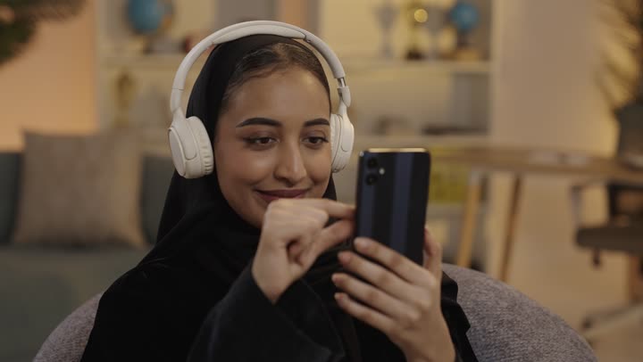 امرأة سعودية تستخدم الهاتف الذكي مع سماعات في المنزل