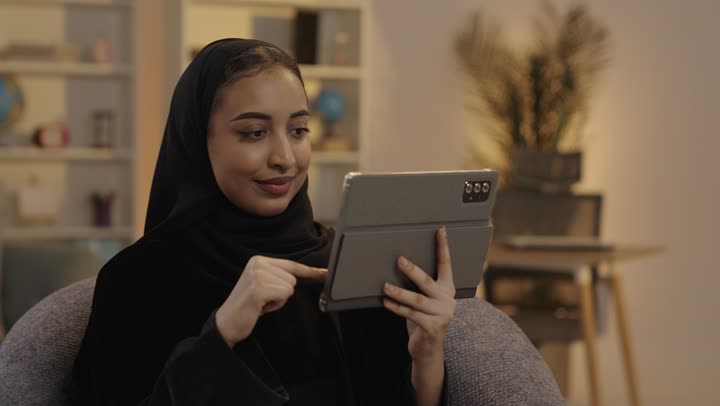 امرأة عربية تستخدم جهاز لوحي في المنزل ليلاً