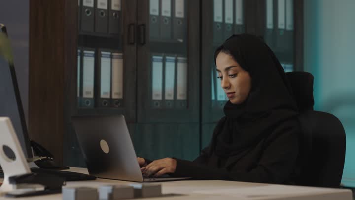 الاستغناء عن الاقلام و الاوراق في تدوين المعلومات و الافكار , امرأة عربية خليجية سعودية ترتدي العباءة السوداء تكتب على جهاز الحاسب الاي المتنقل , الجلوس في غرفة الارشيف , مفهوم التطور في اداء المهام اليومية