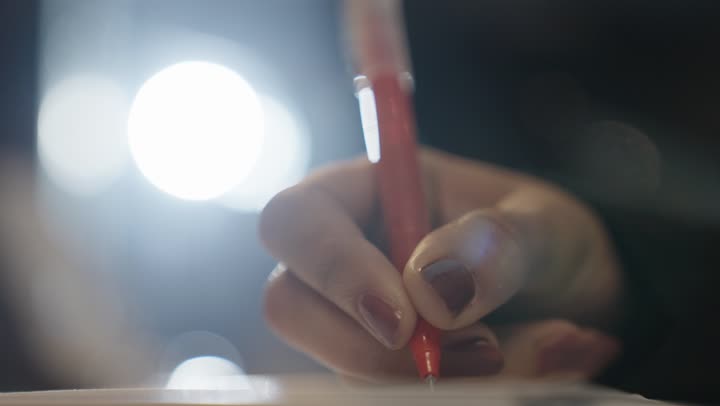A Saudi Arabian Gulf woman wearing a black abaya and a hijab is writing the daily work report using a ballpoint pen, close-up shot.