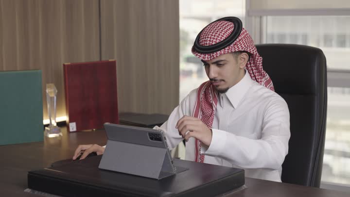 ممارسة العمل اليومي بدقة و احترافية باستخدام الجهاز اللوحي, رجل عربي خليجي سعودي يرتدي الثوب الابيض و الشماغ الملون الاحمر يقوم بتكبير و تقريب الصورة لرؤية اوضح , تحقيق الاستفادة القصوى من الاجهزة التقنية الحديثة