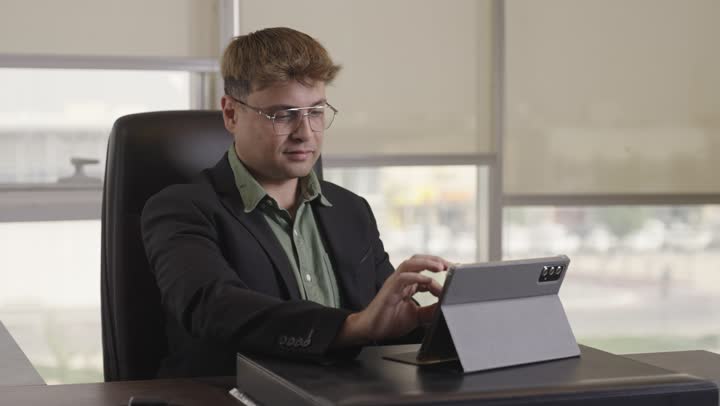 تكبير الصورة على الجهاز اللوحي للتدقيق و التركيز , رجل اجنبي يرتدي البدلة الرسمية يجلس داخل مقر الشركة , ايماءات الموافقة و الاعجاب بالعمل الموجود على الشاشة