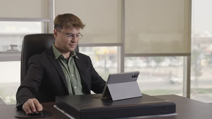 التركيز و الاستغراق في العمل اليومي , رجل اجنبي يرتدي البذلة الرسمية يجلس امام الجهاز اللوحي لحفظ الافكار الخاصة بالمشروع , فأرة حاسب لاسلكية لتسهيل الحركة و تحسين الاداء