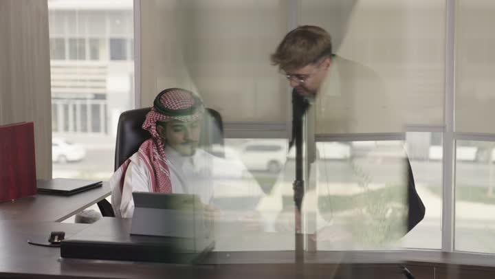 حركة رأس علامة على الموافقة و الفهم , رجل عربي خليجي سعودي يرتدي الشماغ الملون و الثوب الابيض يحرك رأسه بالاعجاب بالرأي المطروح , رجل اجنبي يرتدي البذلة الرسمية و نظارات يشير الى شئ ما في شاشة الجهاز اللوحي