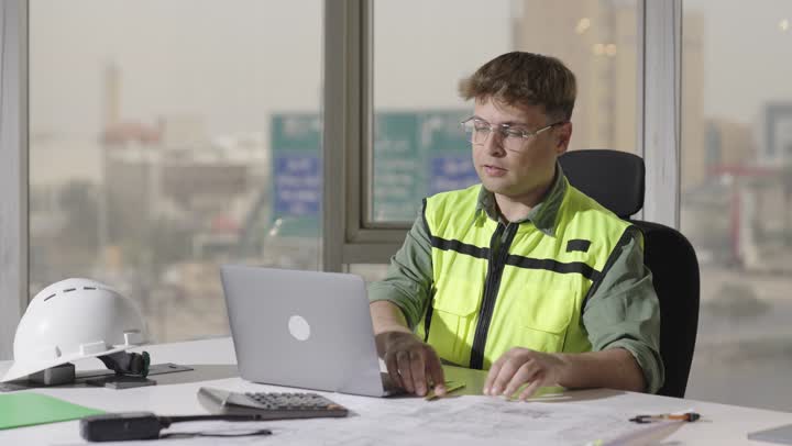 Gestures of happiness and smiles while performing engineering tasks, a foreign architect wearing a reflective safety vest and casual attire taking notes on a laptop.