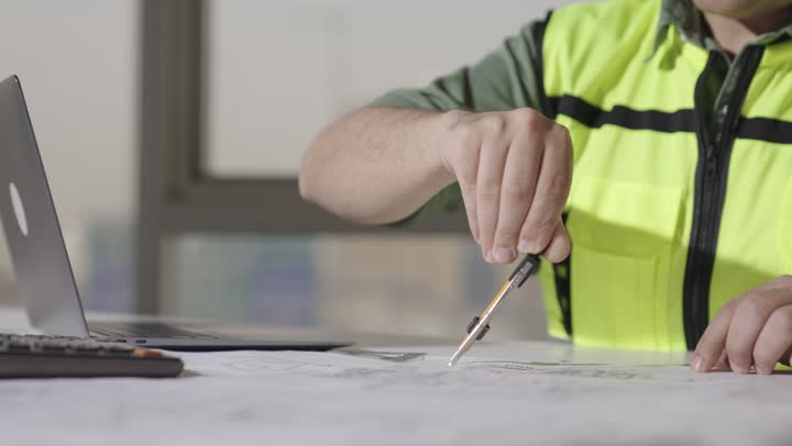 الاعتماد على الادوات الهندسية اليدوية و الاجهزة التقنية الحديثة في مجال الهندسة المعمارية , مهندس اجنبي يرتدي الزي الكاجوال و السترة الواقية يرسم دوائر هندسية بالفرجار , تصوير مقرب