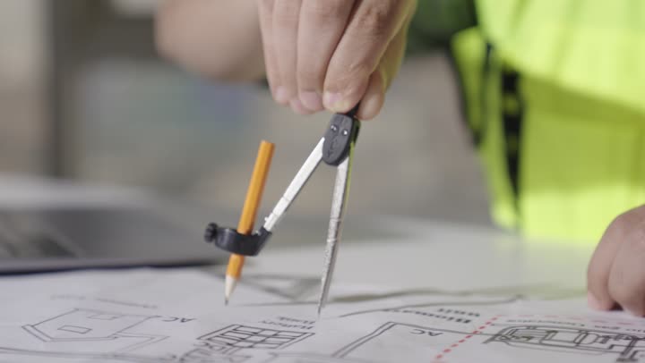 الدقة و التركيز اثناء القيام بالاعمال المطلوبة , مهندس اجنبي يرتدي الزي الكاجوال و السترة الواقية يستخدم الفرجار الهندسي لرسم دائرة , تصوير مقرب