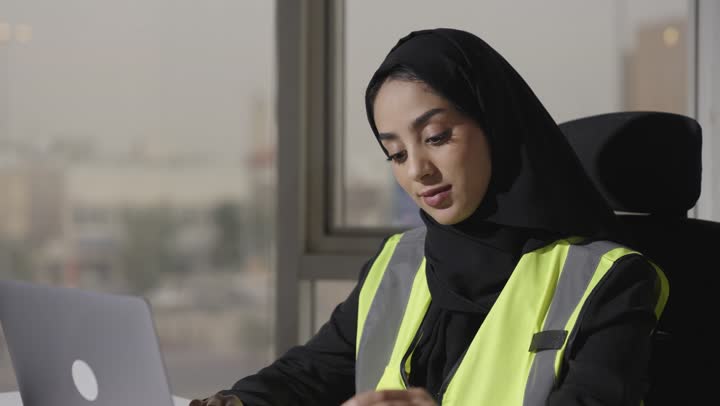 امرأة عربية خليجية سعودية محجبة ترتدي العباءة السوداء تقوم برسم المخططات الهندسية الخاصة بالمشاريع , استخدام الاجهزة الحديثة التقنية مثل الحاسب المتنقل في مجال الهندسة للمساعدة بالعمل بدقة