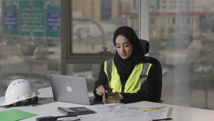 رسم دائرة بالفرجار الهندسي , مهندسة عربية خليجية سعودية محجبة ترتدي عباءة سوداء ترسم المخططات الهندسية باستخدام الاجهزة التقنية الحديثة , الدمج بين الاساليب التقليدية و الحديثة في انجاز المشاريع